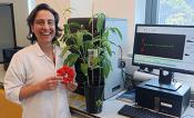 An image of a woman smiling holding a red circle next to a plant and a computer monitor.